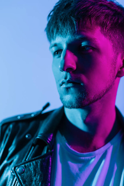 Close-up fashionable color portrait of handsome brutal young man with hairstyle in black leather jacket and white T-shirt in studio with multicolored neon pink light - Fotografie, Obrázek