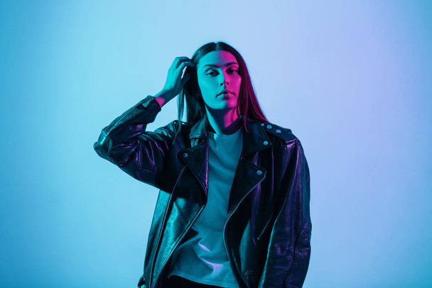 Fashionable beautiful color portrait of a young stylish pretty woman in a fashionable leather jacket in the studio with a multicolored blue pink lights - Fotó, kép
