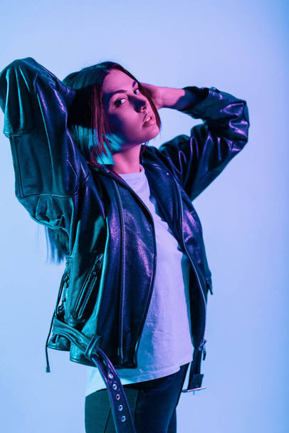 Glamorous beautiful young girl in a black leather jacket and white T-shirt in the studio with bright blue and pink lights. Color portrait of a pretty woman - Photo, Image