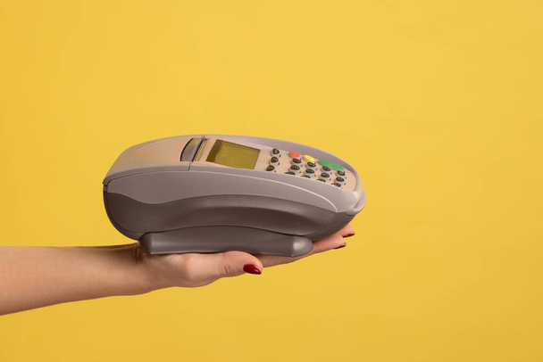 Profile side view closeup of woman hand holding POS or terminal payment or pay pass device. Indoor studio shot isolated on yellow background. - Foto, immagini