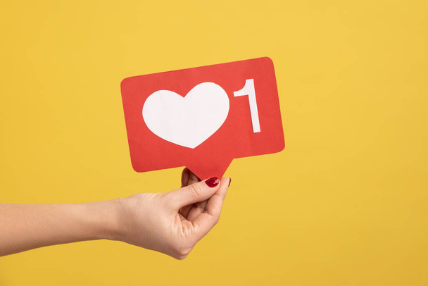 Support interesting web content, push heart button. Closeup of woman hand holding social media like icon, emoji sign to follow subscribe blog. Indoor studio shot isolated on yellow background. - Photo, Image