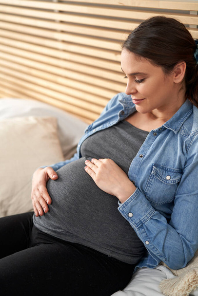 Donna caucasica in gravidanza avanzata seduta sul letto e rilassante - Foto, immagini