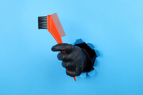 stylist's hand hold hair dye brush through a ragged hole in blue paper. Hair coloring - Foto, afbeelding