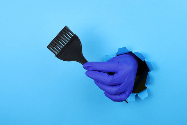 Ręczna szczotka do farbowania włosów stylisty przez dziurę w niebieskim papierze. Farbowanie włosów - Zdjęcie, obraz