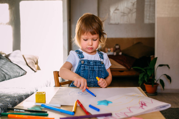 Bambino piccolo a casa al tavolo dei bambini disegna con pennarelli. - Foto, immagini