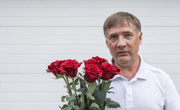 man with flowers on a light background. A gentleman with a bouquet of red roses looks at the camera. - Photo, Image