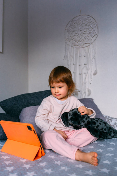 Klein kind kijkt thuis tekenfilms op de bank op de tablet. Technologie voor kindergebruik - Foto, afbeelding