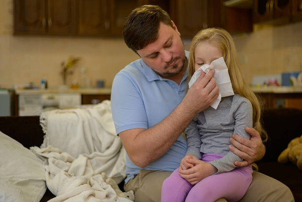 Papa essuie son nez d'enfant malade avec une serviette en papier blanc jetable à la maison. Le père soupçonne sa fille d'être malade. L'enfant ne se sent pas bien. la notion d "égalité dans la famille entre - Photo, image