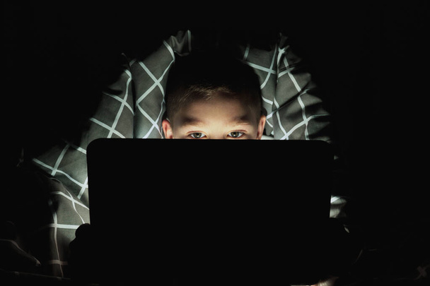 adicción a los artilugios. colegial por la noche con una tableta debajo de las cubiertas. niño jugando juegos por la noche - Foto, Imagen
