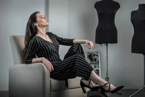 Modèle de fille spectaculaire, couturier assis sur une chaise dans le studio couture vêtements, mode - Photo, image