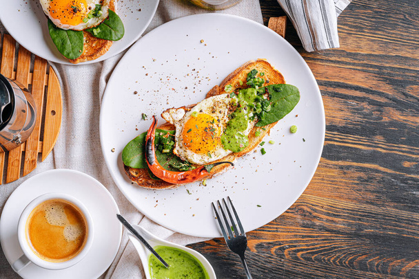 hearty and high-calorie breakfast. delicious and mouth-watering bruschetta with fried eggs and herbs for breakfast with a cup of aromatic coffee. - Foto, Imagen