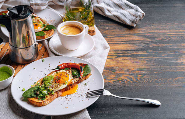 hearty and high-calorie breakfast. delicious and mouth-watering bruschetta with fried eggs and herbs for breakfast with a cup of aromatic coffee. - Foto, Imagen