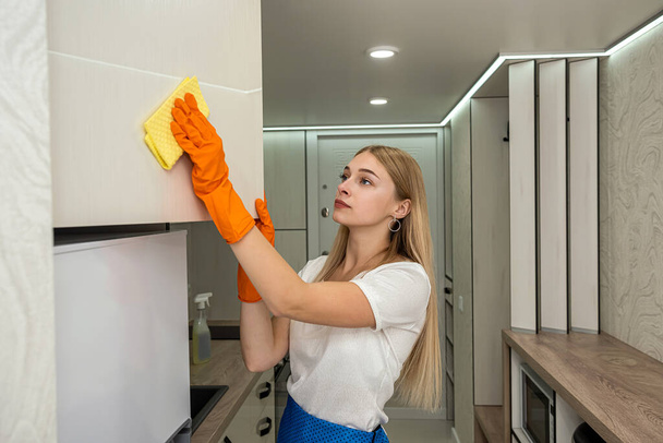 Fiatal háziasszony takarítja a konyhát gumival és speciális spray-vel, zsír és por - Fotó, kép