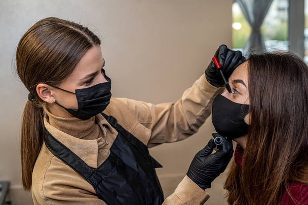 Ein neuer Visagist lud eine junge Kundin in einer speziellen Maske während einer Pandemie zum Make-up ein. Das Konzept der Salons während einer Pandemie - Foto, Bild