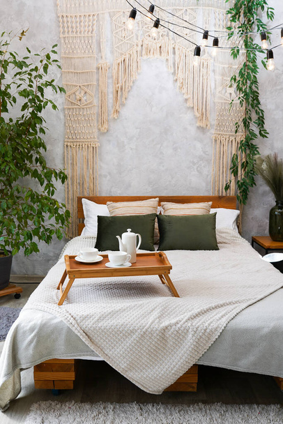 Chambre confortable avec macramé sur lit et tasse de thé, appartement avec design intérieur léger dans un style chic boho - Photo, image