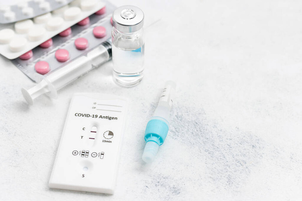 Nopea antigeenitestipakkaus virustaudille COVID-19 positiivisella tuloksella, lääkehoito, pillerit ja lasinen injektiopullo valkoisella taustalla. - Valokuva, kuva