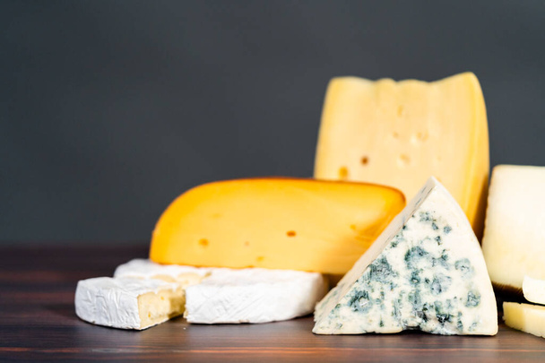 Variety of large gourmet cheese wedges on a dark wooden background. - Fotó, kép