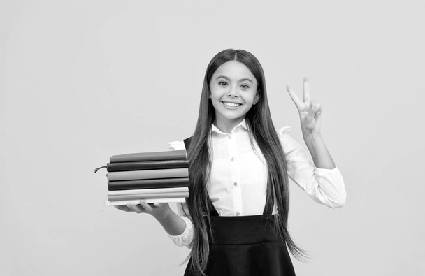 Ευτυχισμένος έφηβος κορίτσι στο σχολείο στολή κρατήσει στοίβα βιβλίο δείχνουν χειρονομία ειρήνης, εκπαίδευση - Φωτογραφία, εικόνα