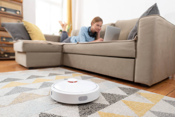 Modern robotic vacuum cleaner. Autonomous robot cleans the apartment, young woman has free time - Foto, afbeelding