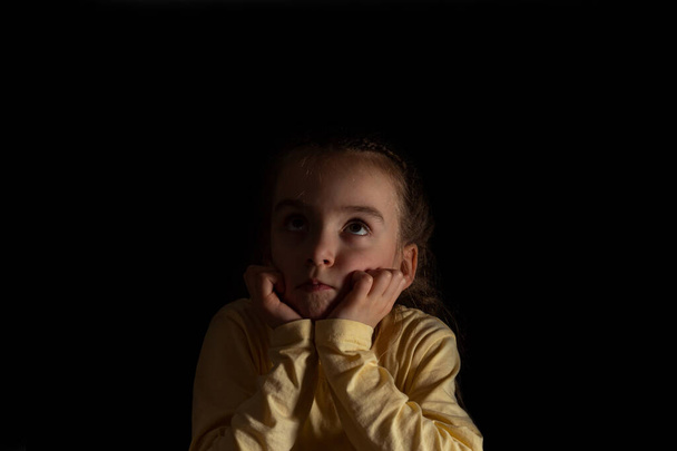 A child on a dark background thinks and dreams - Фото, изображение