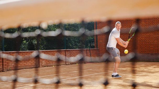 Молодой привлекательный мужчина играет в теннис на оранжевой глине теннисный корт
 - Фото, изображение
