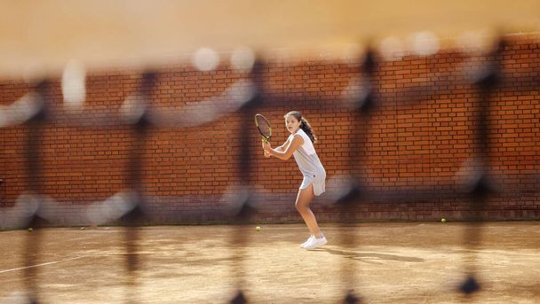Nuori tyttö estää pallon tennismailalla harjoittelun aikana
 - Valokuva, kuva