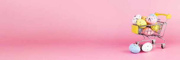 Coloridos huevos de codorniz de Pascua en el carrito de la compra sobre fondo rosa. Copiar espacio. Concepto mínimo de Pascua. Banner - Foto, Imagen