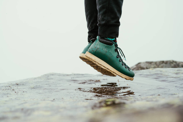 Hiker in boots jumps over a puddle on a fireplace in the mountains. Recreation. A man jumps into a puddle, close up photo of shoes - Photo, Image
