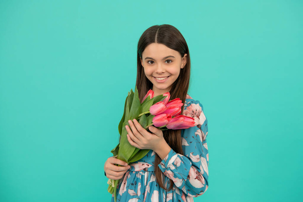 cheerful kid hold flowers for 8 of march. teen girl with spring bouquet on blue background. - Photo, Image