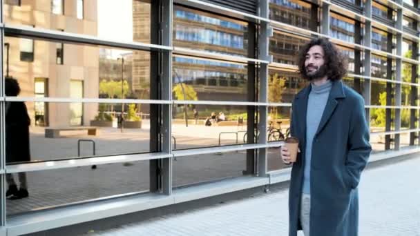 joven empresario hipster sonriendo y caminando con un café en el distrito de negocios - Metraje, vídeo