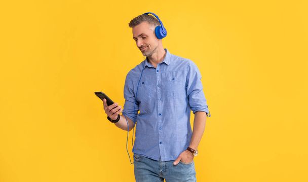 uśmiechnięty dojrzały mężczyzna słuchać muzyki w słuchawkach i rozmawiać przez telefon, komunikacja - Zdjęcie, obraz