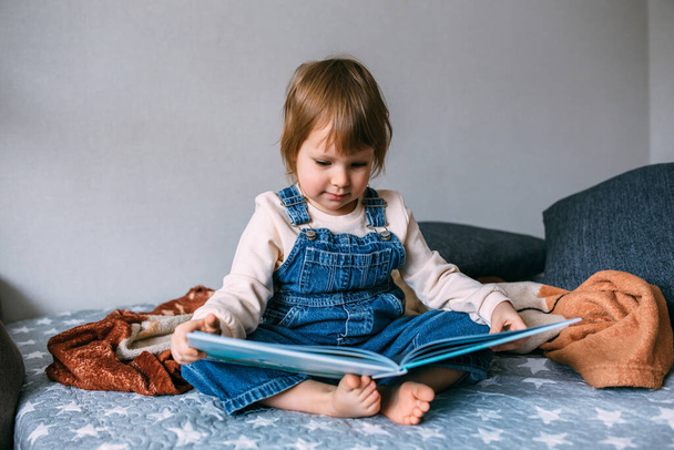 Criança lê seu livro favorito em casa. Kid olha para fotos em contos de fadas. - Foto, Imagem