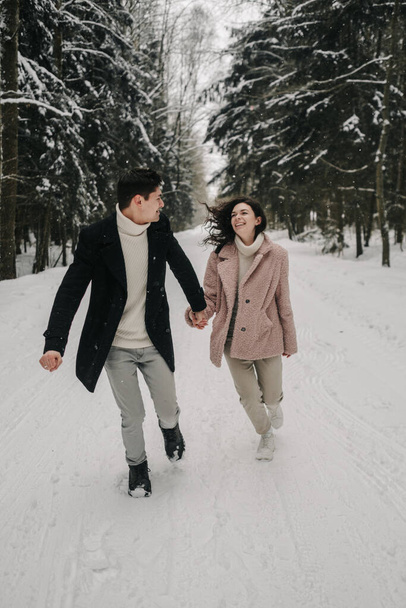 A happy young couple runs along the road in a snowy forest. High quality photo - Foto, imagen