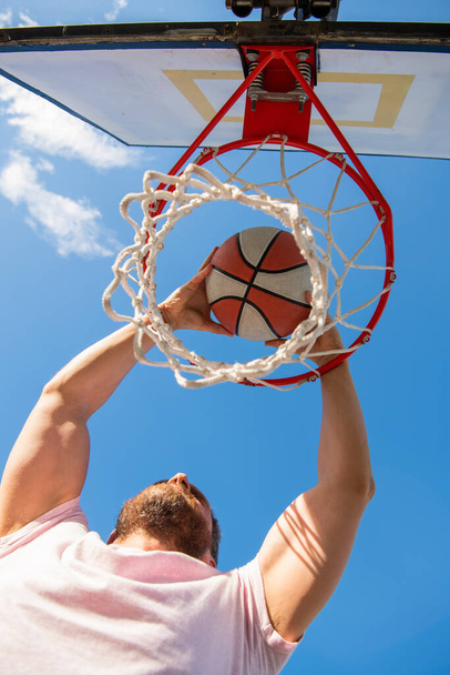 man dunking basketball ball through net ring with hands, sport success - Foto, afbeelding