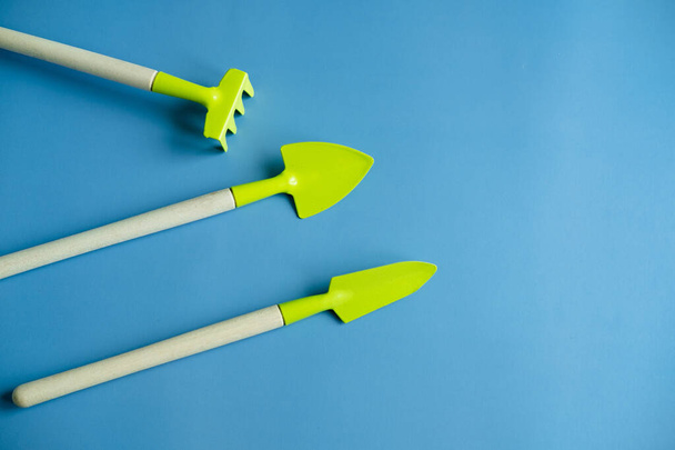 bright green shovel and rake on a blue background top view. Banner. copy spices. flat lay - Fotografie, Obrázek