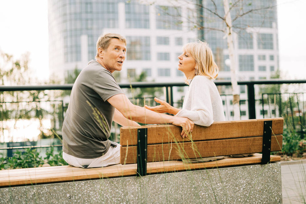 Ein erwachsenes, glückliches romantisches Paar, das verliebt auf einer Bank im Stadtpark sitzt. Ein blonder kaukasischer Mann und eine Frau verbringen Zeit miteinander. Senior Frau und Mann zu Fuß nach draußen. - Foto, Bild