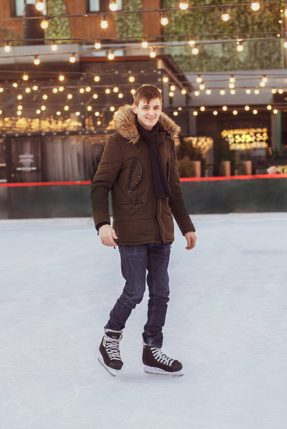 Egy fiatalember korcsolyázik a korcsolyapályán, a kamerába néz és mosolyog.. - Fotó, kép
