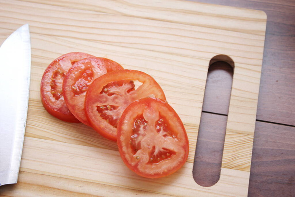 Нарезанные помидоры и ножи помещаются на деревянную доску в деревянном столе. - Фото, изображение