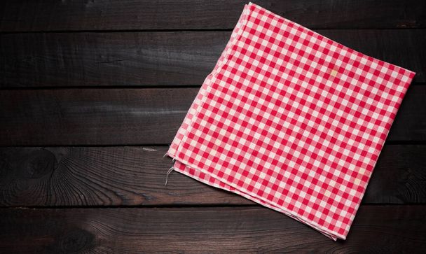 folded red and white cotton kitchen napkin on a wooden brown background, top view, copy space - Фото, зображення