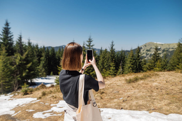 Woman in casual clothes while walking in the mountains makes a photo on a smartphone camera - Photo, Image