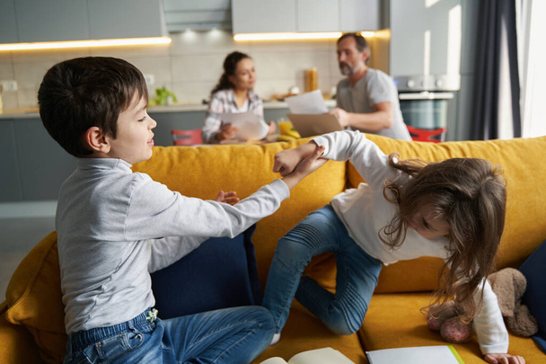 Children playing on sofa with parents in background - Foto, immagini