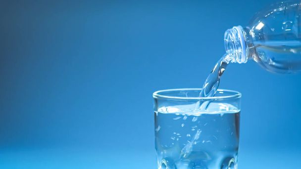 スタジオショットきれいな飲料水がガラスと自然の青の背景に注ぎ込まれました。健康的な飲料水の概念 - 写真・画像