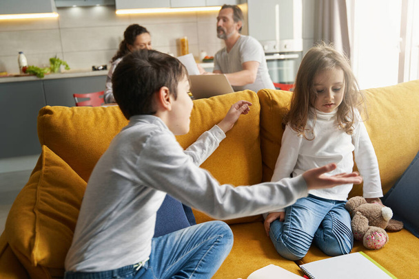 Boy telling something to his little sister on sofa - Valokuva, kuva