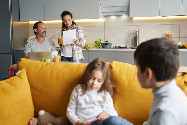 Female checking paper near husband with kids on sofa - Photo, Image