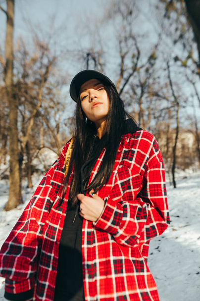 Portret van een stijlvolle dame in een hemd en pet op een zonnige winterdag in een besneeuwd park en poserend voor de camera. - Foto, afbeelding