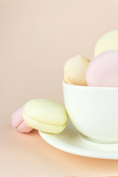 Francouzské delikátní marshmallows dezert na snídani v porcelánu bílý šálek kávy hrnek na pastelové béžové pozadí - Fotografie, Obrázek