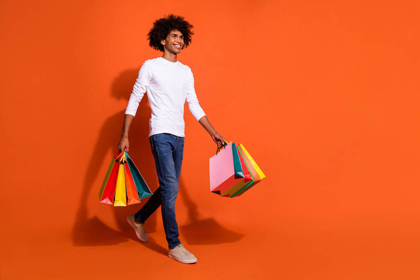 Photo of cool dreamy guy wear white shirt jumping holding bargains walking empty space isolated orange color background - Φωτογραφία, εικόνα