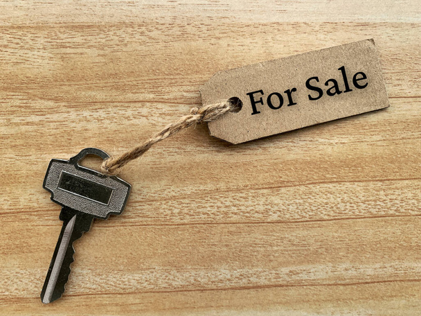 Tekst na brązowym tagu z kluczem domu i drewnianym tle stołu - Na sprzedaż. Pojęcie własności. - Zdjęcie, obraz