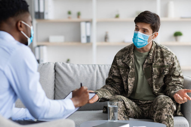 Emotional soldier in face mask visiting psychologist while pandemic - Φωτογραφία, εικόνα