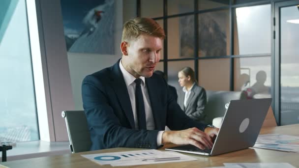Un giovanotto in giacca e cravatta che lavora con un portatile in ufficio. Uomo d'affari alla scrivania con computer portatile - Filmati, video